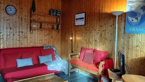 A cozy room with a red sofa, a wooden chair, a TV, and a clock on the wall. - 1st floor, view mountain, tv, 50m², Montgenèvre (Montgenèvre)