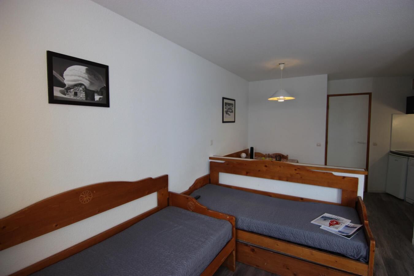 A small, compact room with two wooden bunk beds, a single bed, a small table, and a refrigerator.