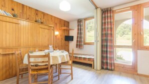 Una habitación con paneles de madera, una mesa redonda con sillas, un banco y un televisor montado en la pared.