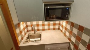 Una cocina compacta con un lavamanos de acero inoxidable, un microondas y un lavavajillas integrados en los armarios.
