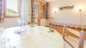 Una habitación acogedora con una mesa redonda lista para comer, un banco de madera y una cama con colcha escocesa.