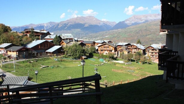 Un pueblo montañoso con casas de madera, un campo cubierto de césped y una vista despejada de montañas lejanas.