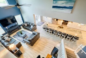 Uma sala de estar moderna com uma televisão grande, sofá de couro e uma área de jantar com cadeiras brancas.