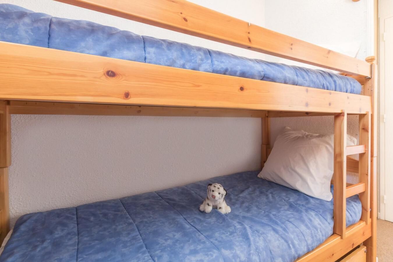 Un lit superposé avec un matelas bleu et un petit jouet en peluche sur le lit du bas.