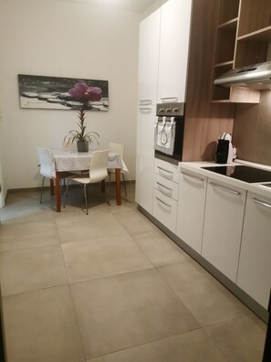 A compact kitchen with white cabinets, a built-in oven, and a coffee machine.