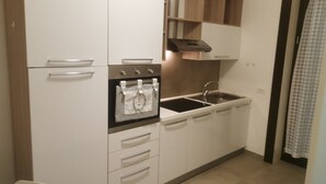 Una cucina compatta con mobili bianchi, forno in acciaio inossidabile, lavello e ripiano in legno sopra il bancone.