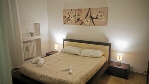 Un letto rifatto con copria letto, due lampade ai comodini, un termosifone e un quadro appeso al muro.