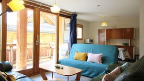 A cozy living room with a blue sofa, a wooden coffee table, and a dining area with a table and chairs. - 100m from ski slopes, 1st floor, balcony, parking, tv, 54m², Montgenèvre (Montgenèvre)