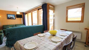 A dining area with a table set for four, a green sofa, and a window with curtains. - 100m from ski slopes, 1st floor, balcony, parking, tv, 54m², Montgenèvre (Montgenèvre)