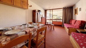A cozy room with a dining table set for four, a sofa, and a window with curtains. - 50m from ski slopes, 2nd floor, balcony, tv, 38m², Les Menuires (Les Menuires)