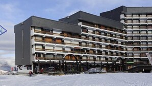 A multi-story hotel with a modern architectural design, featuring balconies and a ski lift visible in the foreground. - 50m from ski slopes, 2nd floor, balcony, tv, 38m², Les Menuires (Les Menuires)