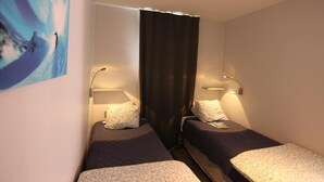 A small, well-lit room with two single beds, each with a pillow and a bedside lamp. - 150m from ski slopes, Ground floor, balcony, 29m², Val Thorens (Val Thorens)