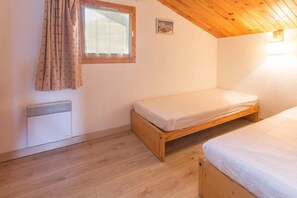 Une petite pièce accueillante, avec deux lits en bois, une fenêtre avec des rideaux, un radiateur et un tableau accroché au mur.