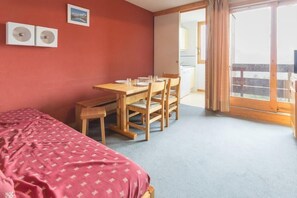 Une pièce comprenant un lit, une table à manger avec des chaises, une petite table et une porte-fenêtre coulissante donnant sur un balcon.