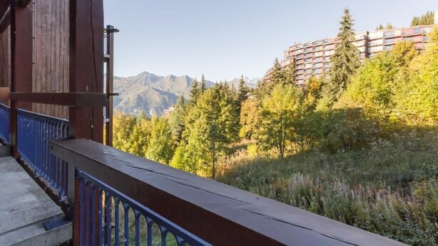 Un bâtiment en bois doté d’un balcon donnant sur un paysage montagneux et une zone boisée.
