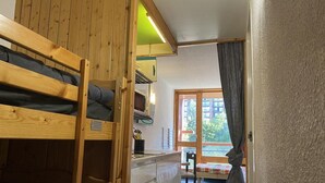 Une chambre compacte avec un lit superposé, un coin cuisine et une vue sur l’extérieur par une fenêtre.