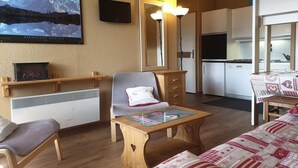 Ein gemütliches Wohnzimmer mit einer Couch, einem Holztisch und einem an der Wand befestigten Fernseher.