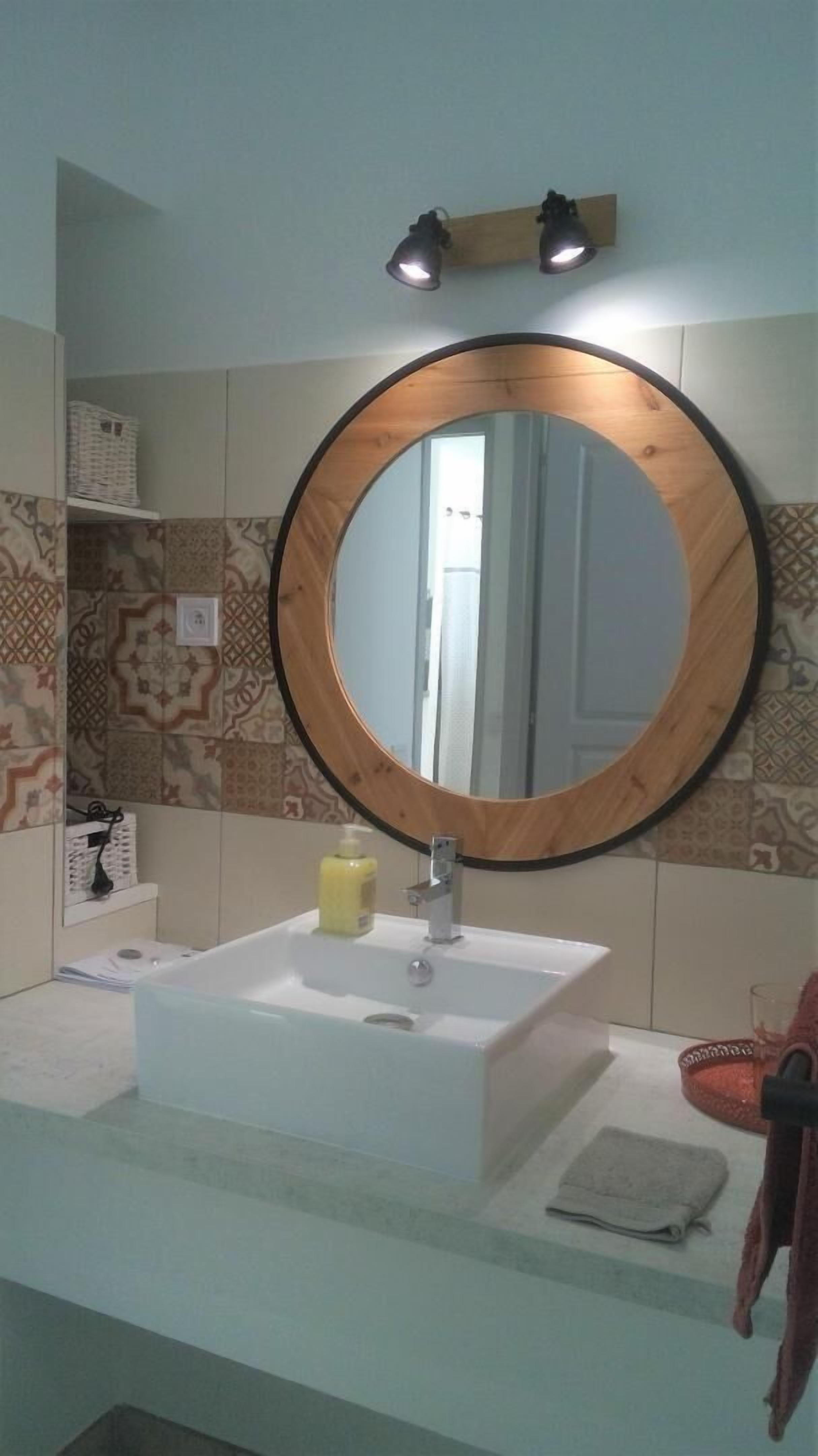 A bathroom with a round mirror, a white sink, and patterned tiles on the wall.
