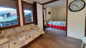 Une pièce avec un canapé à motifs, un lit recouvert d’une couette rouge et blanche, et une horloge murale.