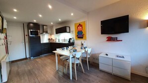Une cuisine moderne avec un coin repas, un téléviseur à écran plat fixé au mur et un petit meuble blanc.