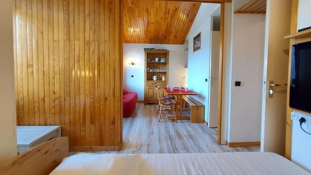 Un dormitorio con techo de madera, una cama, un armario de madera y vista al comedor con una mesa y sillas.