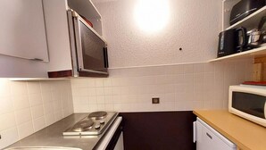 Una cocina compacta con estufa, microondas, lavamanos y un refrigerador pequeño.