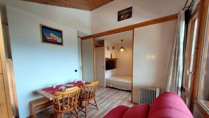 Una habitación acogedora con un sofá rojo, una mesa de comedor de madera con sillas, un televisor pequeño y una ventana con cortinas.