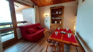Una habitación acogedora con un sofá rojo, una mesa de comedor de madera con sillas y una estantería.