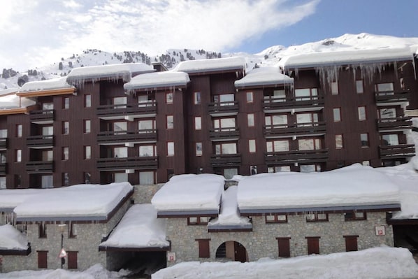 A multi-story building with snow-covered roofs and balconies, surrounded by snow-covered mountains.