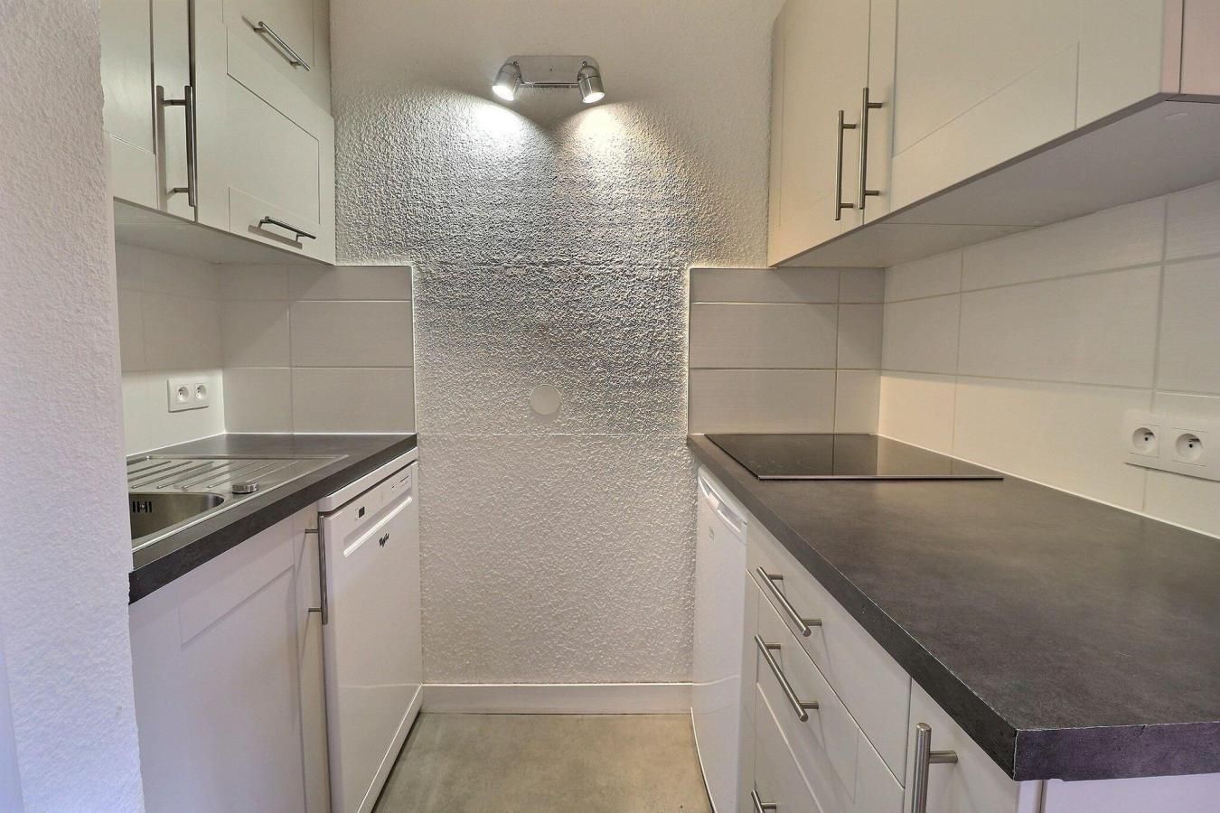 A compact kitchen with white cabinets, a stainless steel countertop, and a textured backsplash.