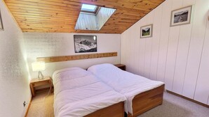 A bedroom with a wooden bed, a nightstand, a lamp, and a skylight. - 10m from ski slopes, 3rd floor, balcony, 43m², Méribel-Mottaret (Méribel - Les Allues)