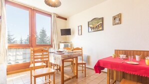 A dining area with a table set for two, a television on the wall, and a window with curtains. - 10m from ski slopes, 1st floor, view valley, swimming pool, tv, ski locker, 24m², Le Corbier (Le Corbier)