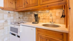 A kitchen with wooden cabinets, a stove, a microwave, and a sink. - 10m from ski slopes, 1st floor, view valley, swimming pool, tv, ski locker, 24m², Le Corbier (Le Corbier)