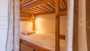 A bunk bed with a wooden frame and a white mattress. - 10m from ski slopes, 1st floor, view valley, swimming pool, tv, ski locker, 24m², Le Corbier (Le Corbier)
