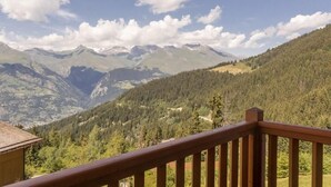 Paisaje montañoso con una terraza de madera y vistas a montañas lejanas.