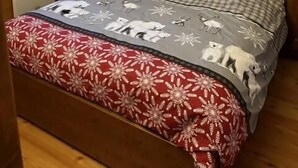Una cama de madera con un edredón a cuadros y una manta roja con estampado floral.