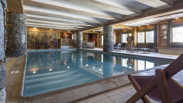 Una piscina interior con pilares de piedra, vigas de madera y suelo de baldosas.