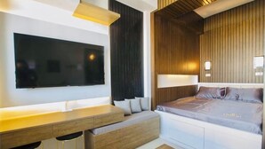 Ett modernt hotellrum med en stor platt-TV, en vägg med träpanel som ger rummet karaktär, en säng med ett grått madrass och ett inbyggt skrivbord med pallar.