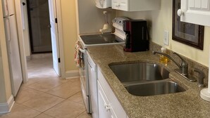 Una cocina con armarios blancos, encimeras de granito, un lavamanos doble, microondas, cafetera y refrigerador.