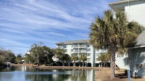Un lago tranquilo que refleja un edificio de varios pisos, rodeado de árboles y un cielo despejado.