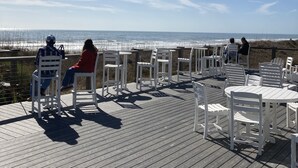 Ett trädäck med vita stolar och bord med utsikt över en strand.