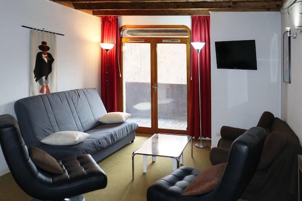 A living room with a sofa, armchairs, a coffee table, a TV, and a sliding door leading to an outdoor area.
