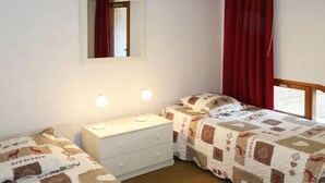 Ein Schlafzimmer mit zwei Betten, einem Schminktisch, einem Spiegel und roten Vorhängen.