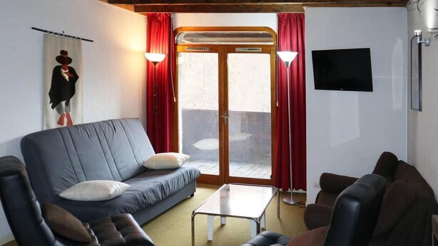 Ein Wohnzimmer mit einer Couch, Sesseln, einem Couchtisch und einer Schiebetür zu einem Außenbereich.