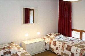 A bedroom with two beds, a dresser, a mirror, and a window with red curtains. - Ski-in/ski-out & foot of the slopes, 6th floor, view resort, balcony, 40m², Les Orres (Les Orres)