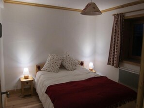 Une chambre à coucher avec un lit, deux lampes de chevet, une fenêtre avec des rideaux et une tête de lit en bois.