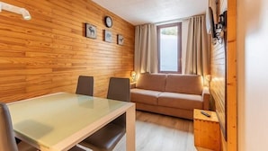 Una habitación con pared de madera, un sofá, una mesa con sillas y un reloj.