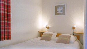 A neatly made bed with two pillows, a small bedside table with a lamp, and a framed picture on the wall. - 10m from ski slopes, 33m², Méribel-Mottaret (Méribel - Les Allues)