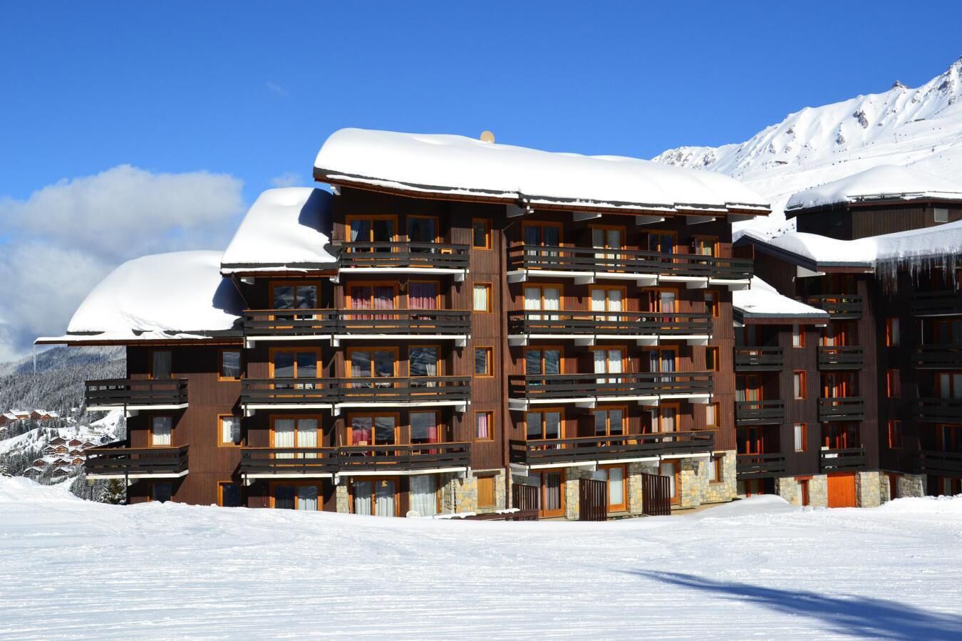 A multi-story hotel with balconies, set against a snowy mountain backdrop.