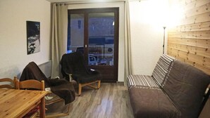 A compact living space with a wooden floor, a sofa, a chair, a table, and a view through a glass door. - Ski-in/ski-out & foot of the slopes, 7th floor, view valley, balcony, tv, 26m², Les Orres (Les Orres)